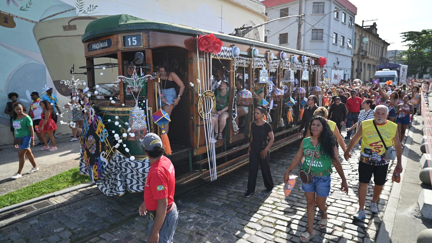 Bonde histórico nº 15, decorado para o CarnaBonde 2026, avança pela rua de paralelepípedos do Centro Histórico de Santos acompanhado por foliões fantasiados.